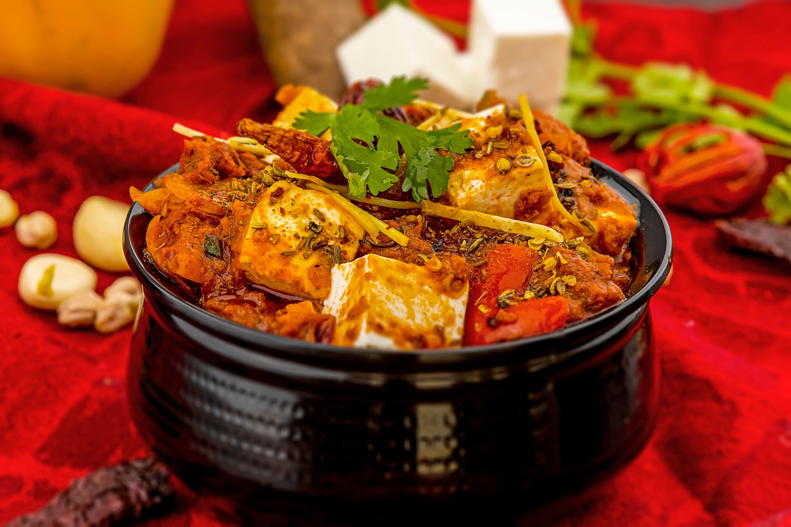 Spicy paneer tikka masala garnished with cilantro and spices on a vibrant red background.