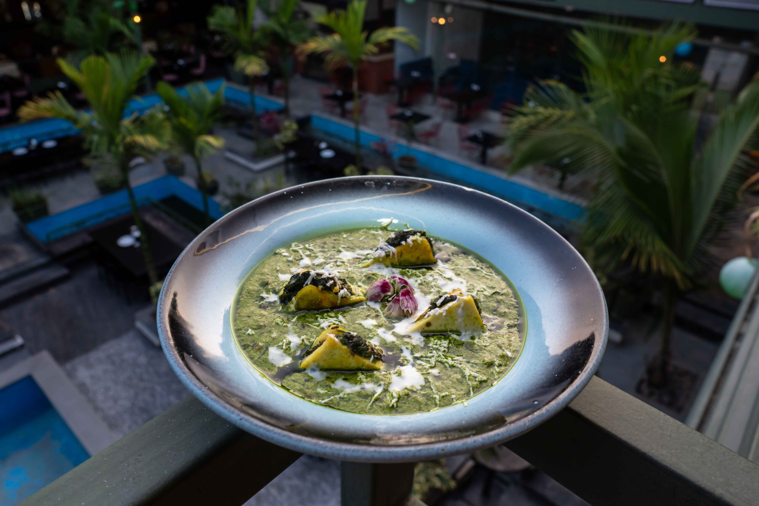 A gourmet Indian dish garnished with cream and spinach served at a rooftop restaurant with a tropical backdrop.