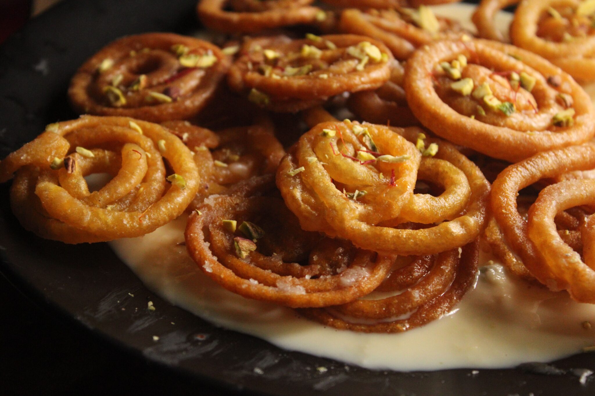 Closeup of freshly prepared Indian jalebi with pistachio garnish.